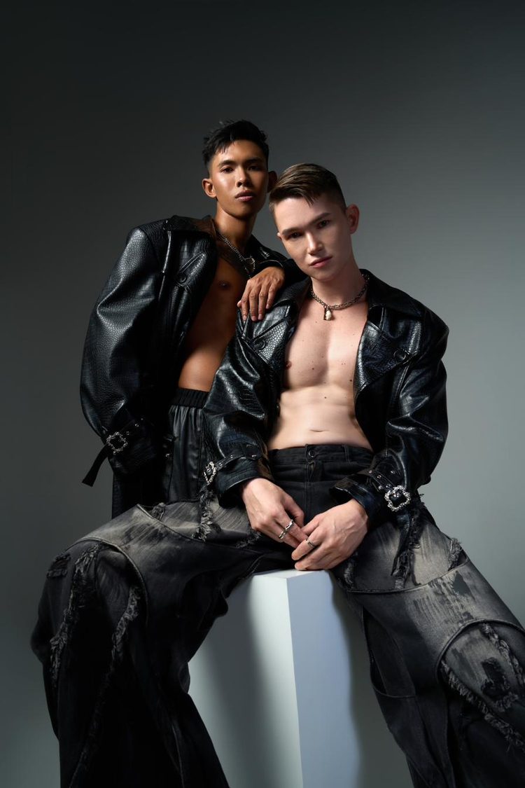 Dee Mak and a second model in black leather jackets and distressed denim on a dark studio backdrop