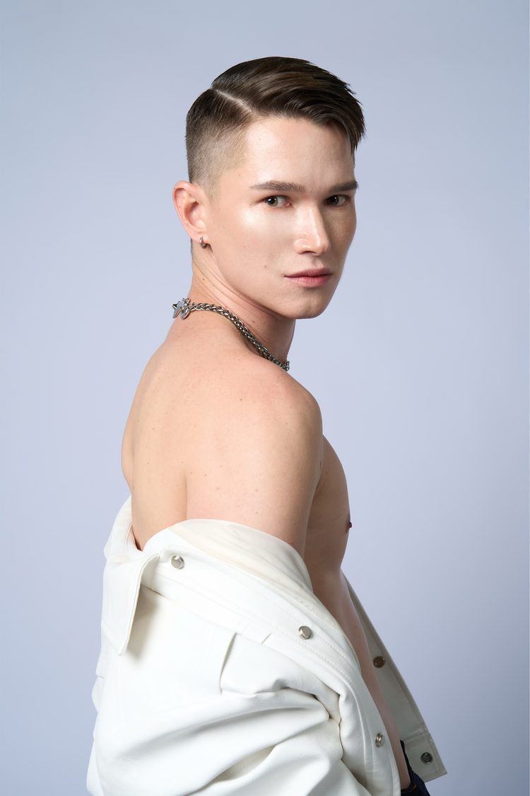 Dee Mak shirtless in profile, white leather jacket dropped off one shoulder, silver chain necklace and hoop earring