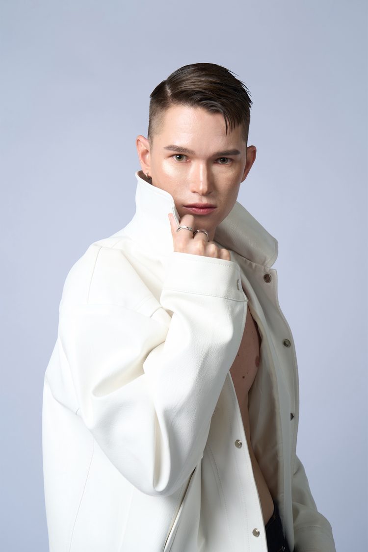 Dee Mak close portrait in a white leather jacket with a raised collar, hand at his chin