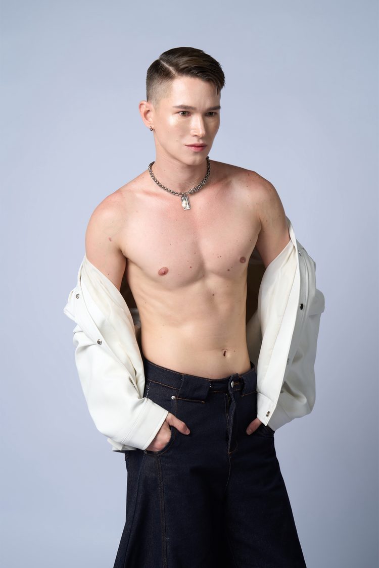 Dee Mak shirtless with the white leather jacket dropped to his elbows, silver pendant necklace, looking away from camera