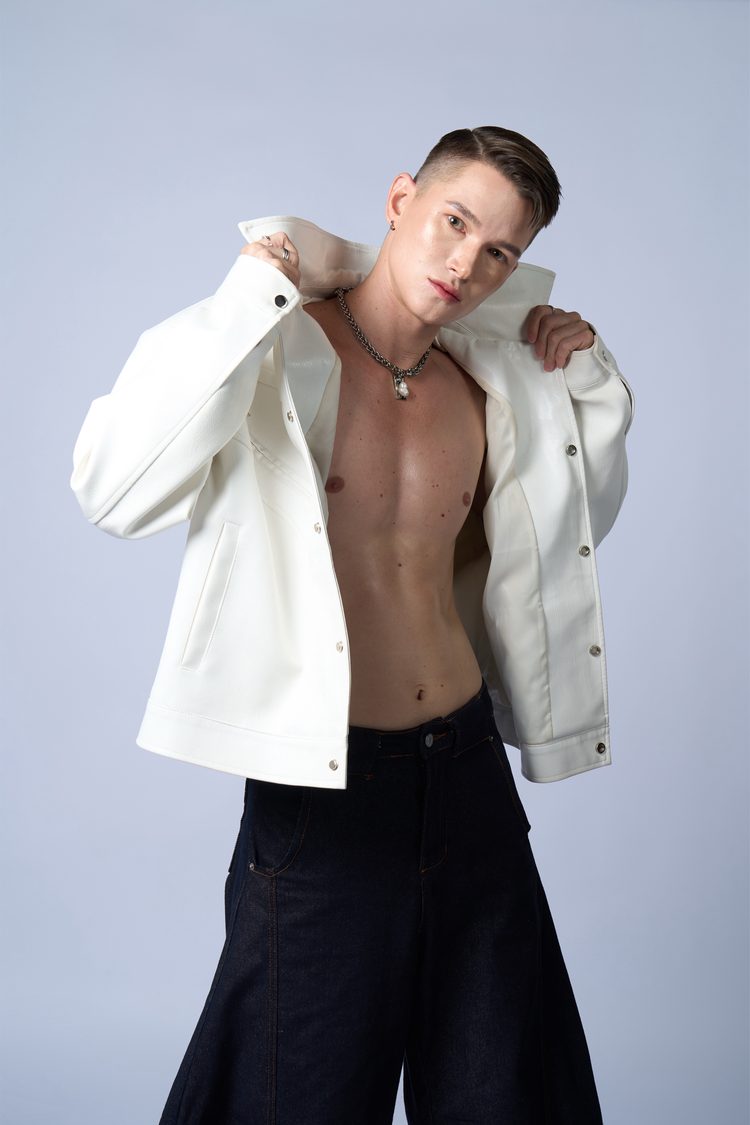 Dee Mak with the white leather jacket draped over one shoulder, hands raised to the collar, chain necklace